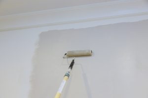 Male hand painting wall with paint roller painting apartment, renovating with color paint